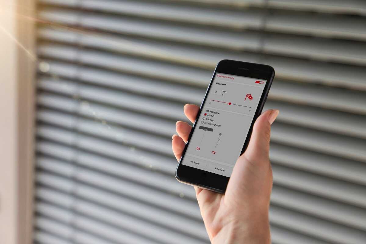Moderne Jalousiesteuerung per Smartphone-App Smartphone mit Steuerungsapp für Jalousien vor Fenster
